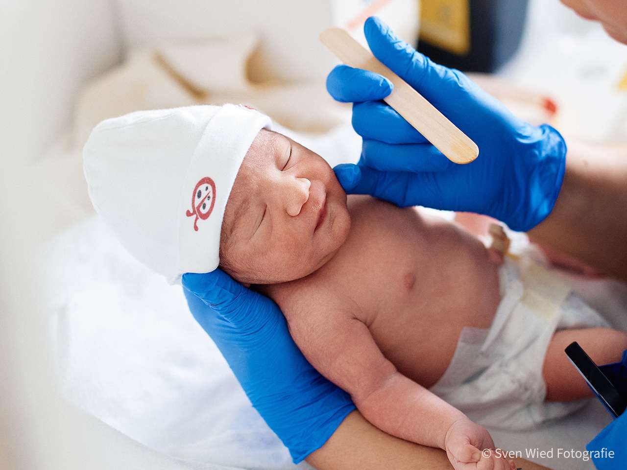 A newborn baby is being examined by a person wearing blue gloves.