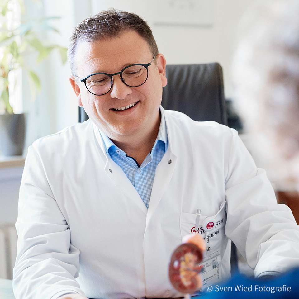 Doctor in a white coat smiles during a conversation with a patient who is only seen from behind.