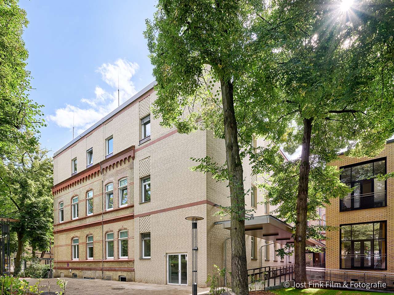 Two buildings surrounded by trees under a blue sky, one with a traditional facade, the other modern.