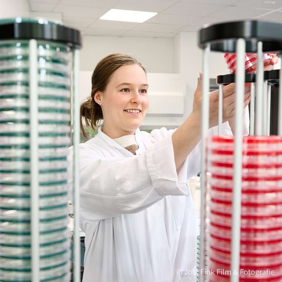 A laboratory assistant in a white coat sorts Petri dishes in a modern laboratory.