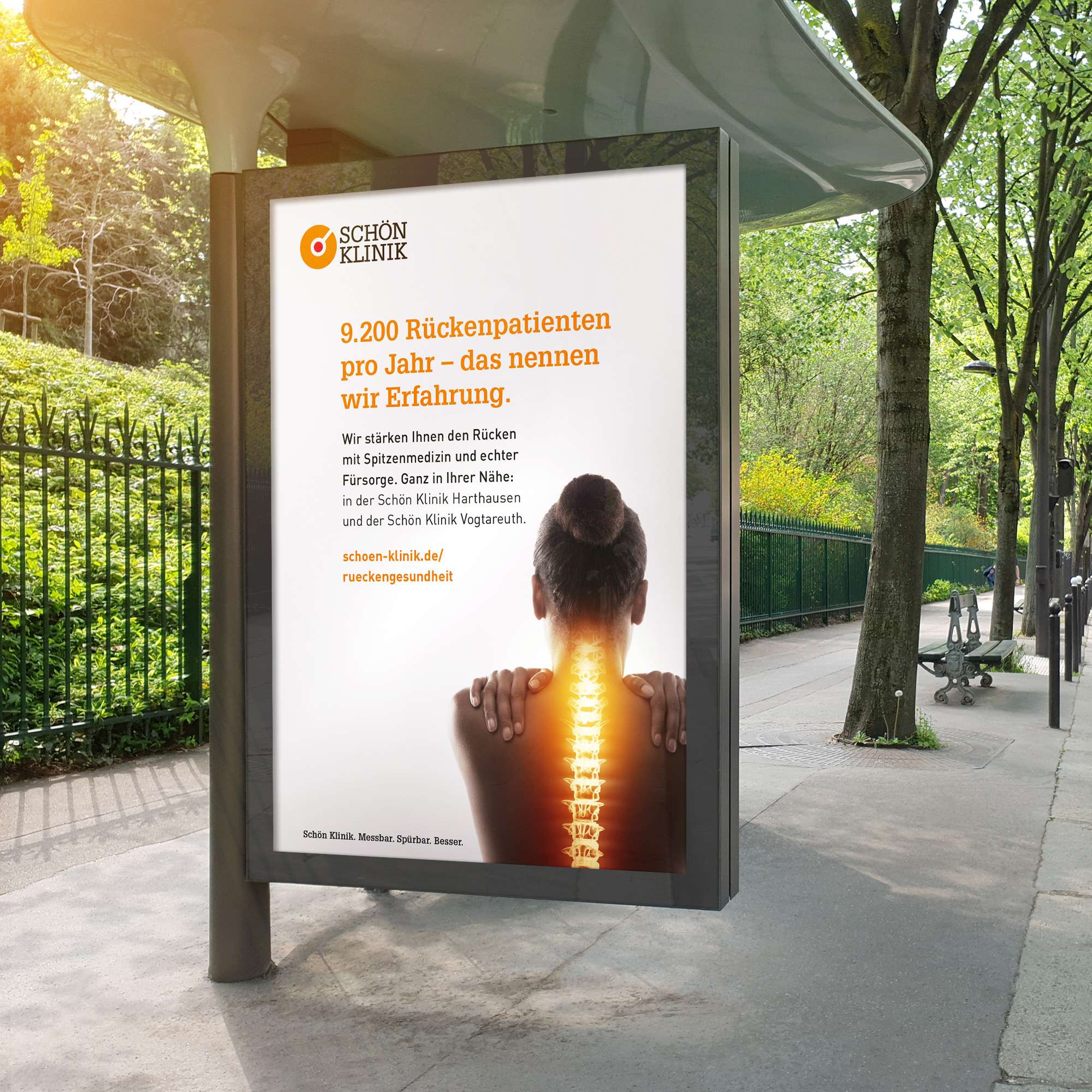 Plakat aus der Akquisekampagne der Schön Klinik an einer Bushaltestelle vor einem Park inkl. dem Keyvisual (eine Frau in der Rückenansicht, deren Wirbelsäule orange hervorgehoben ist, daneben ein kurzer Text, der beschreibt, dass die Schön Klinik 9.200 Rückenpatienten pro Jahr betreut und dementsprechend viel Erfahrung hat) und der Hauptnavigation