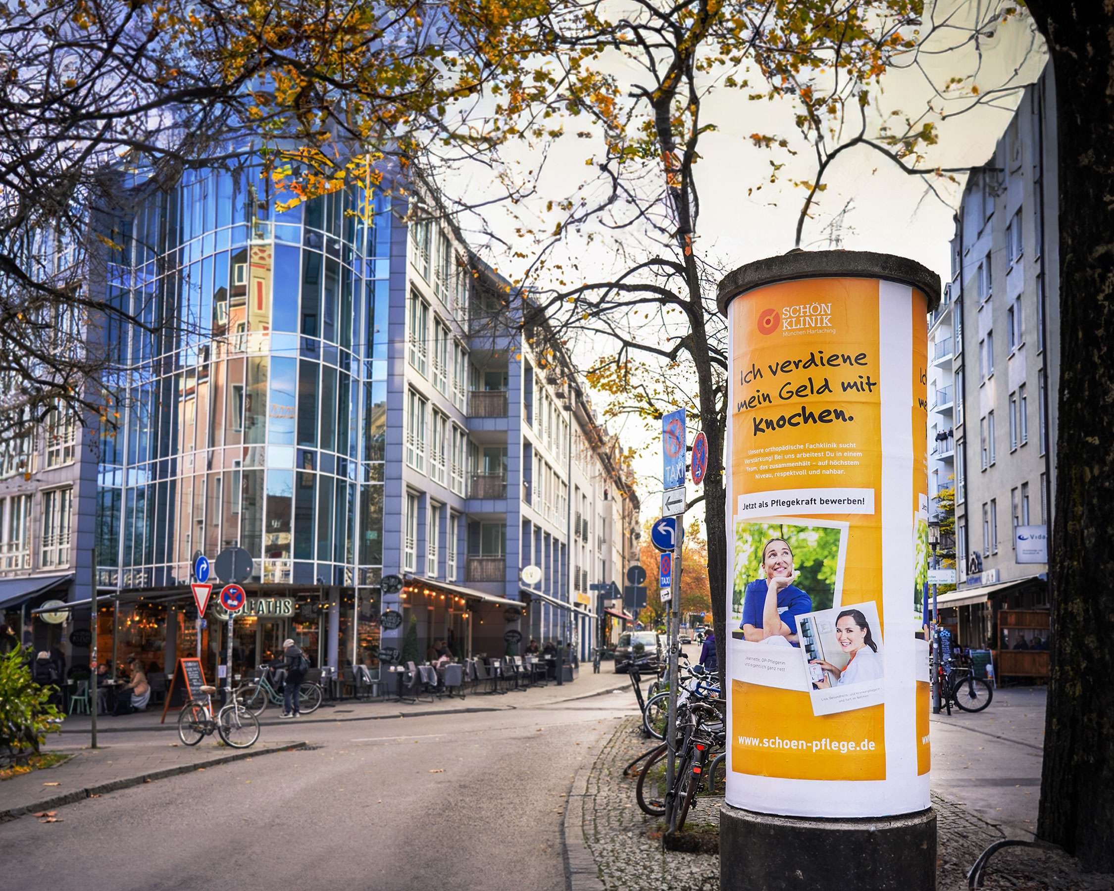 Litfasssäule in der Münchner Innenstadt mit Plakatierung aus der Personalkampagne der Schön Klinik: Zwei Polaroid-Bilder von Pflegekräften unter dem Claim 